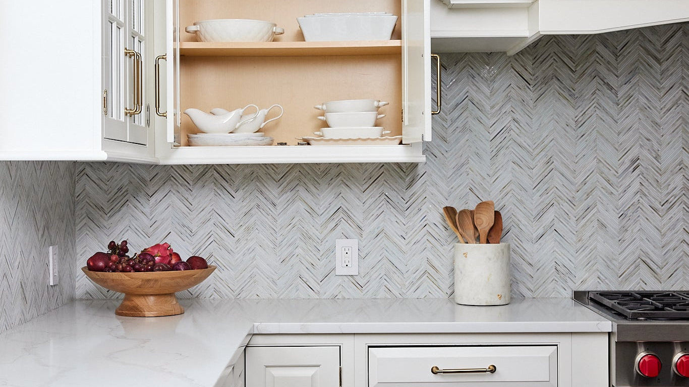 Kitchen with open cabinet displaying bowls, countertop with fruit bowl and utensils, and stove.