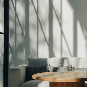 Modern interior with a sofa and coffee table in front of large windows casting shadows on the wall.