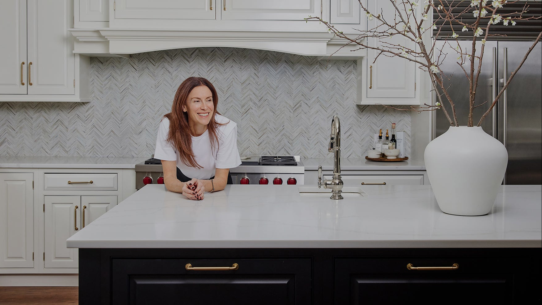 Woman sitting at a kitchen island with white cabinets and modern appliances.