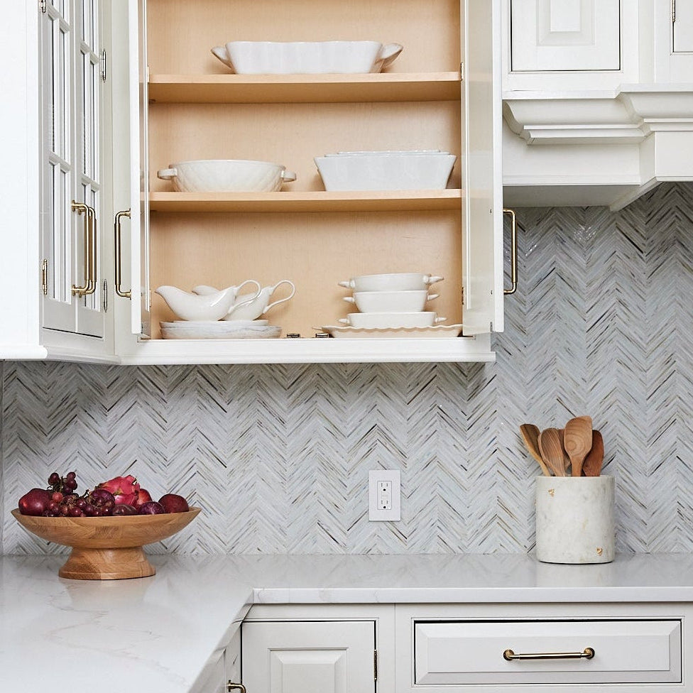 Alyssa Lane - Kitchen Reset:
Open kitchen cabinet with dishes, fruit bowl, and utensils on a countertop with a chevron patterned backsplash.