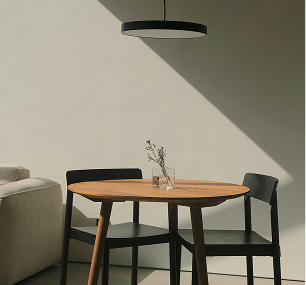 Round wooden table with two black chairs in a minimalistic room.