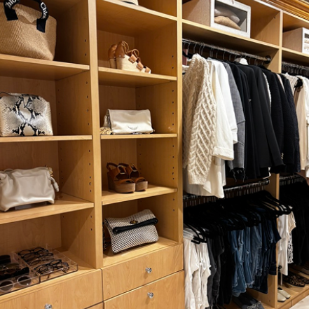 Closet with wooden shelves containing bags and shoes, and clothes hanging on racks.
