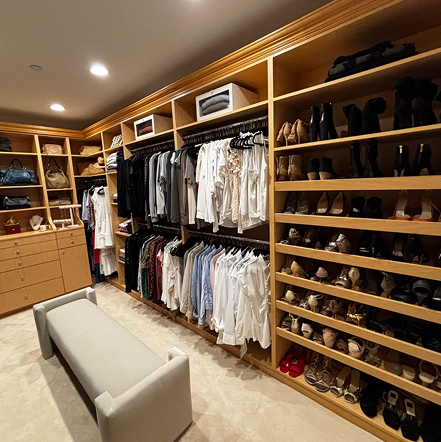 Modern walk-in closet with wooden shelves, clothes, and shoes.