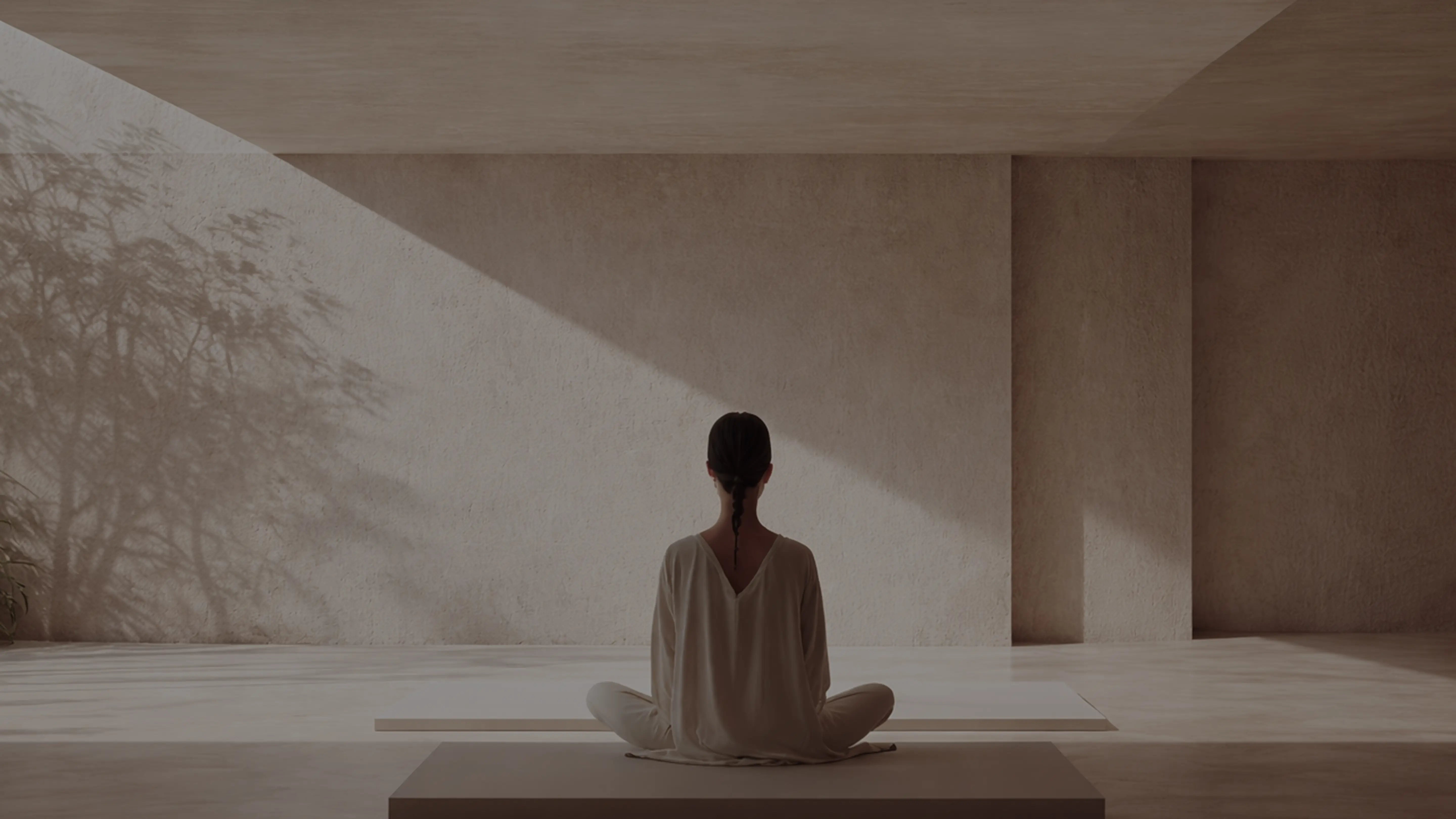 Person sitting in a meditative pose in a minimalist indoor setting with soft lighting.