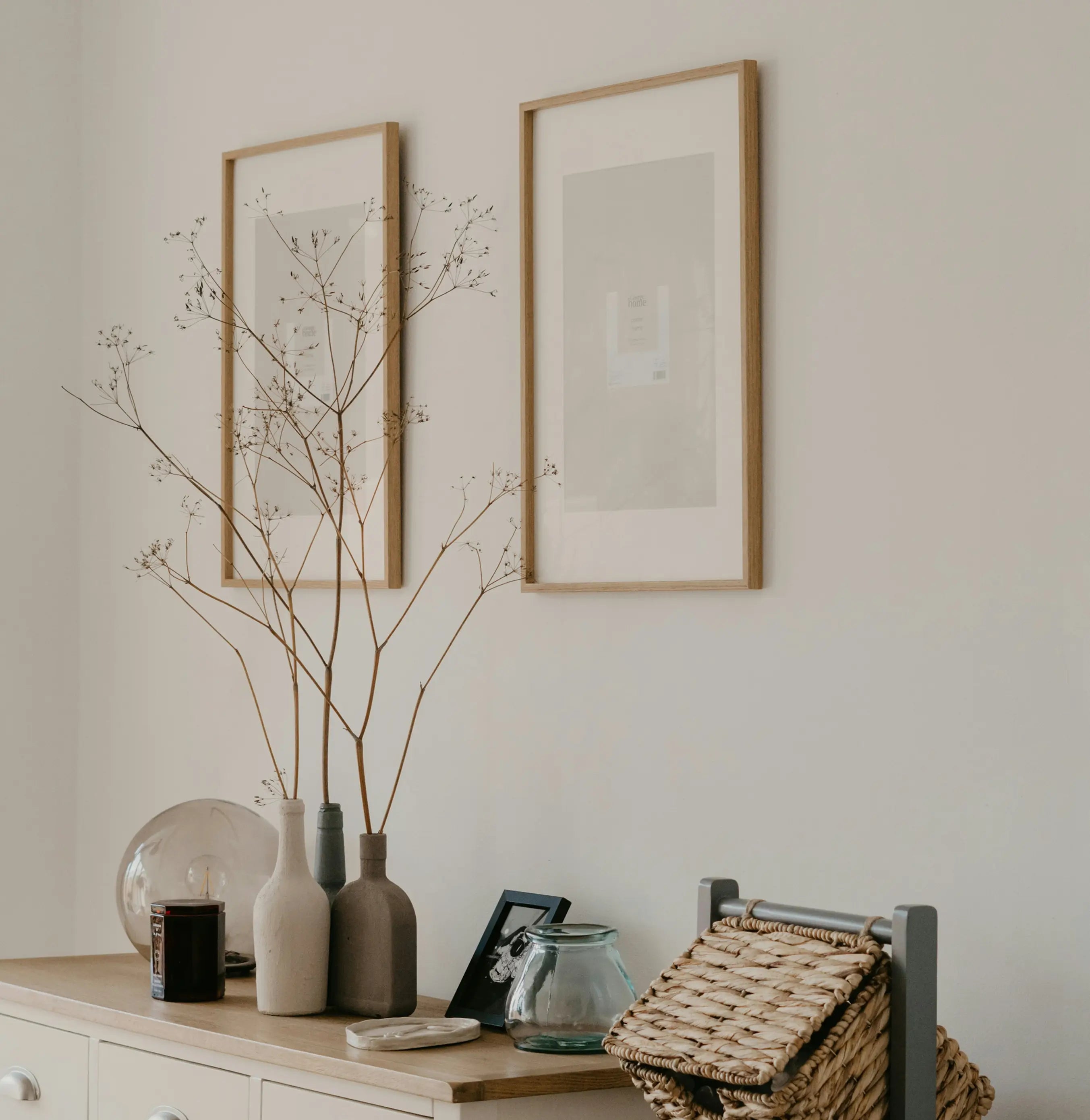 Decorative setup with framed art, vases, and a basket on a shelf against a neutral wall.
