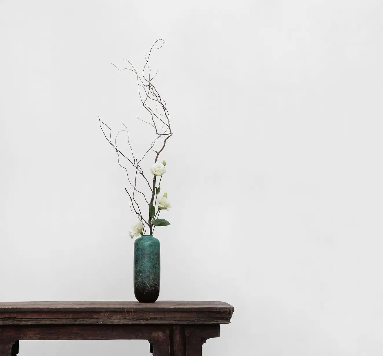 Teal vase with branches and flowers on a wooden table