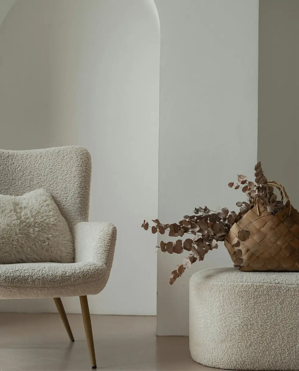 Modern interior with textured armchair, round ottoman, and woven basket with dried plants.